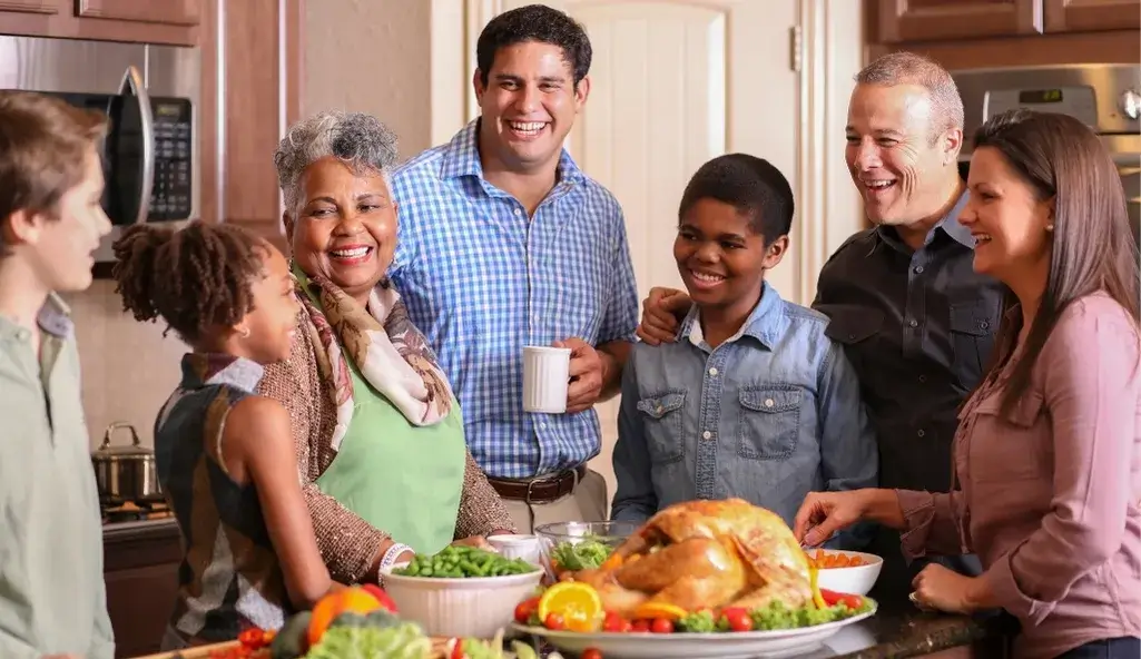 Multigenerational family smiling around Thanksgiving dinner table with roasted turkey.